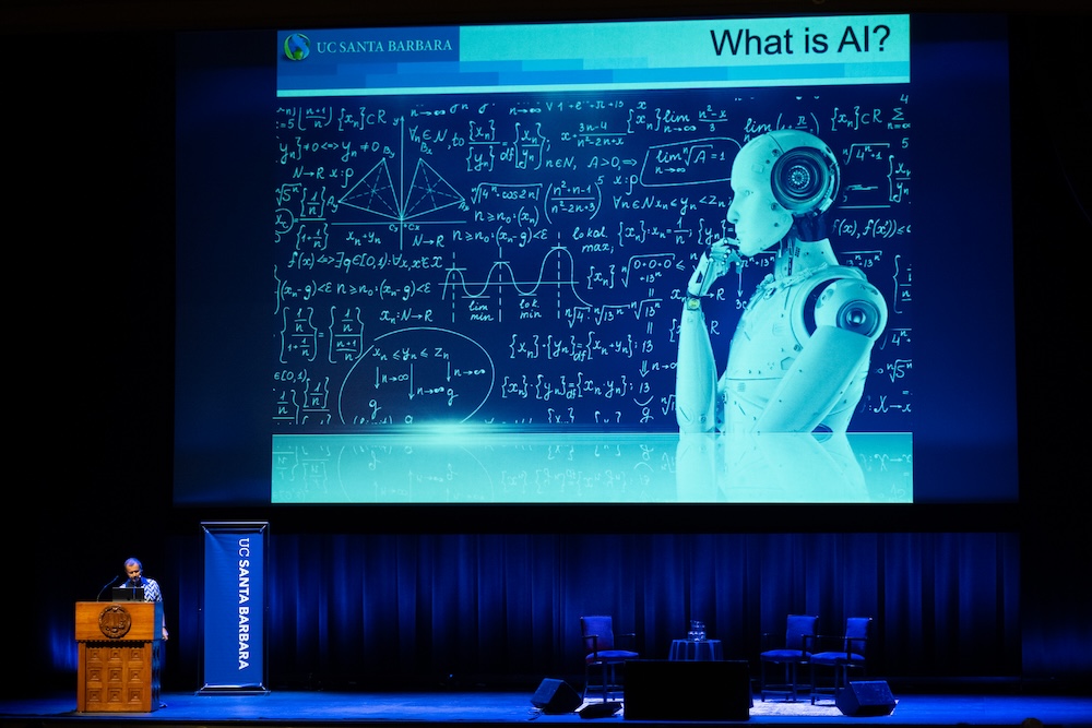 Speaker presenting at the 2026 Economic Summit with a slide titled “What is AI?” displayed on stage.